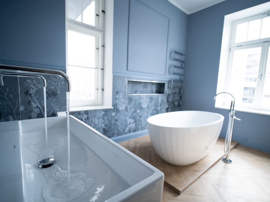Waschtisch mit Wandarmatur, dahinter eine freistehende Badewanne
